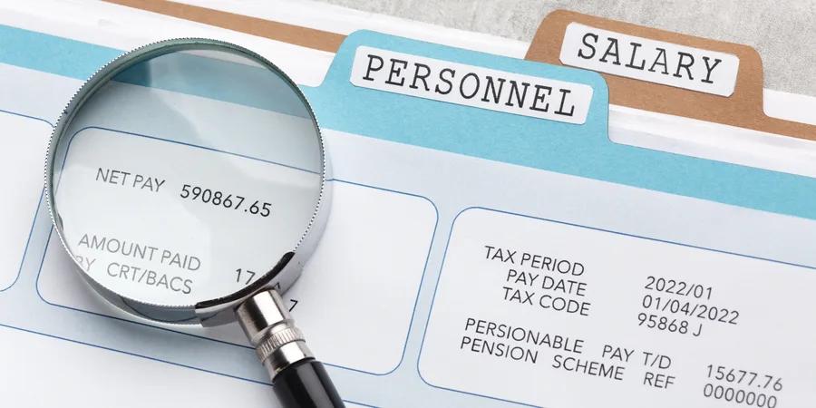 Magnifying glass examining a payslip showing net pay, in a personnel and salary filing folder