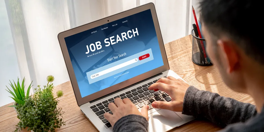Person typing on a laptop displaying a job search website with a search bar